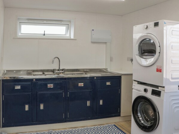 A compact kitchen with a built-in washing machine, a window above the sink, and a patterned rug. - Singletree Cottage (Warminster)