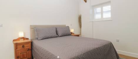 Un dormitorio con cama, mesitas de noche de madera, una ventana con persianas y un ventilador de techo.