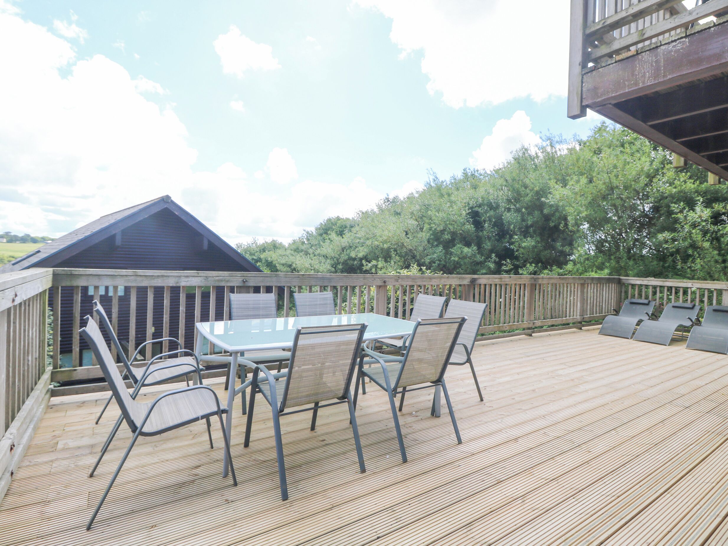A wooden deck with a table and chairs, a small shed, and a view of trees and sky.