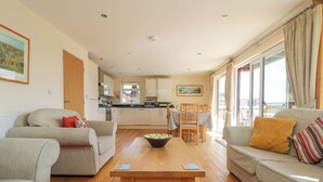 A modern living room with a wooden coffee table, two sofas, and a dining area with a table and chairs. - The Willows (St. Columb Major)