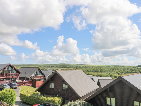 A row of wooden cabins with sloped roofs, a paved driveway, and a view of green hills under a partly cloudy sky.