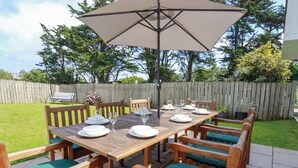 A wooden patio table with a large umbrella, surrounded by wooden chairs with green cushions.