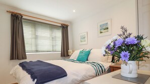 A bedroom with a bed, a nightstand, a vase with flowers, and a window with curtains.