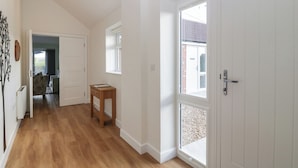 A hallway with wooden flooring, white walls, and a door leading to a room. - Doubletree Cottage (Warminster)