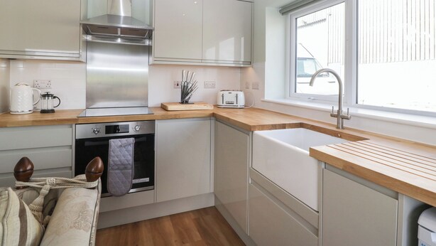 A modern kitchen with white cabinets, a stainless steel range hood, a built-in oven, and a window providing natural light. - Doubletree Cottage (Warminster)