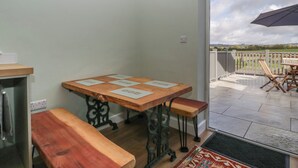 A room with a wooden table and bench, a door leading to an outdoor patio with a view. - Doubletree Cottage (Warminster)