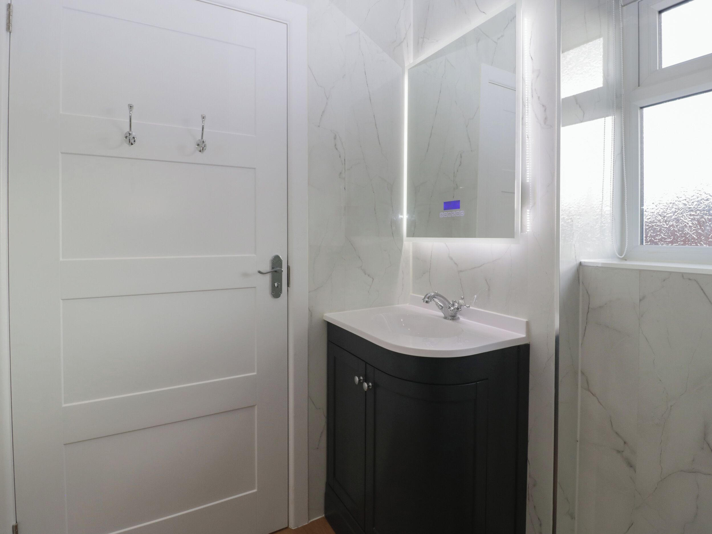 Une salle de bain avec une porte blanche, un lavabo surmonté d’un miroir et une fenêtre.