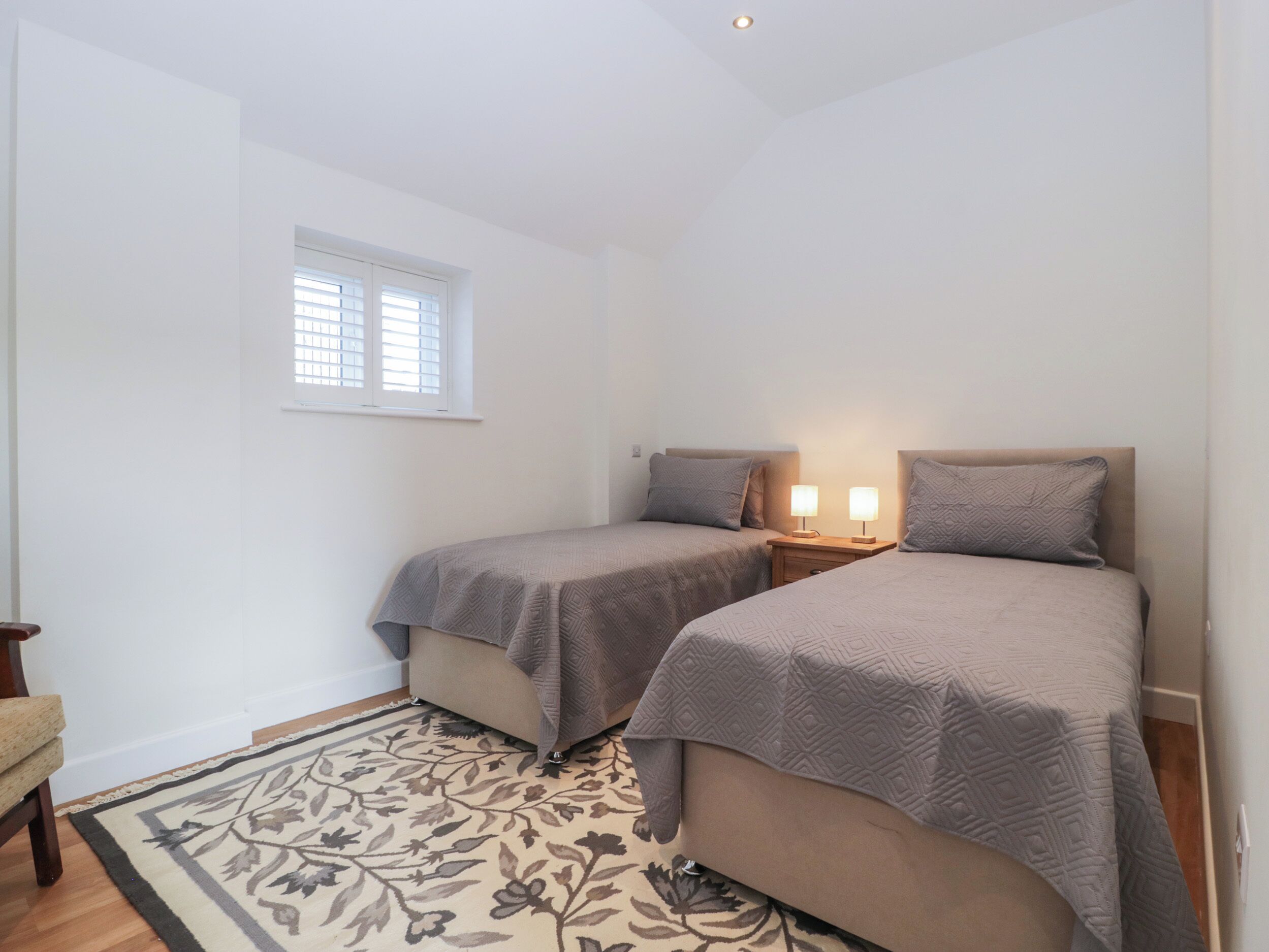 Een slaapkamer met twee bedden, een raam, een nachtkastje met lampen en een bloemenkleed.