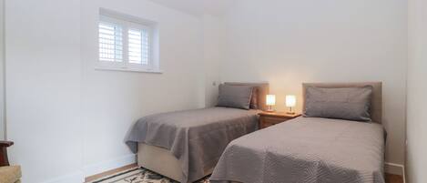 Een slaapkamer met twee bedden, een raam, een nachtkastje met lampen en een bloemenkleed.