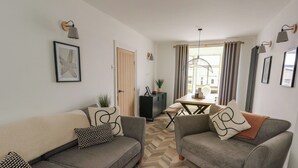 Ein modernes Wohnzimmer mit zwei grauen Sofas, einem Parkettboden mit Zickzackmuster und einem Essbereich mit Tisch und Stühlen.