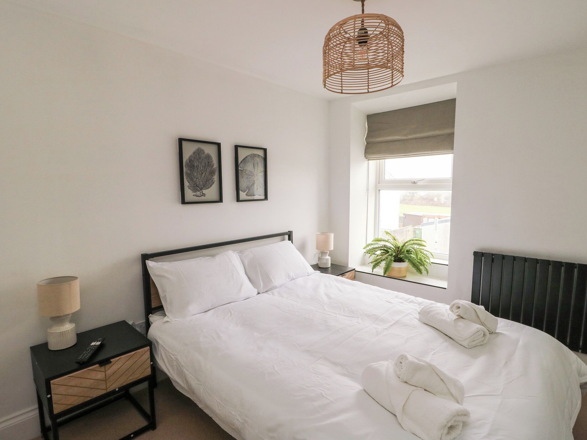 A neatly made bed with white linens, a bedside lamp, a small plant, and two framed pictures on the wall.