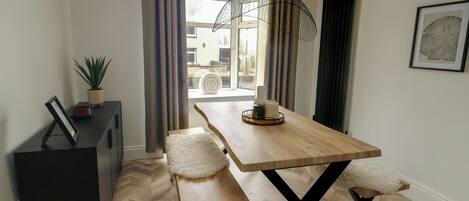 A modern dining area with a wooden table, benches, a potted plant, and a view through the window.
