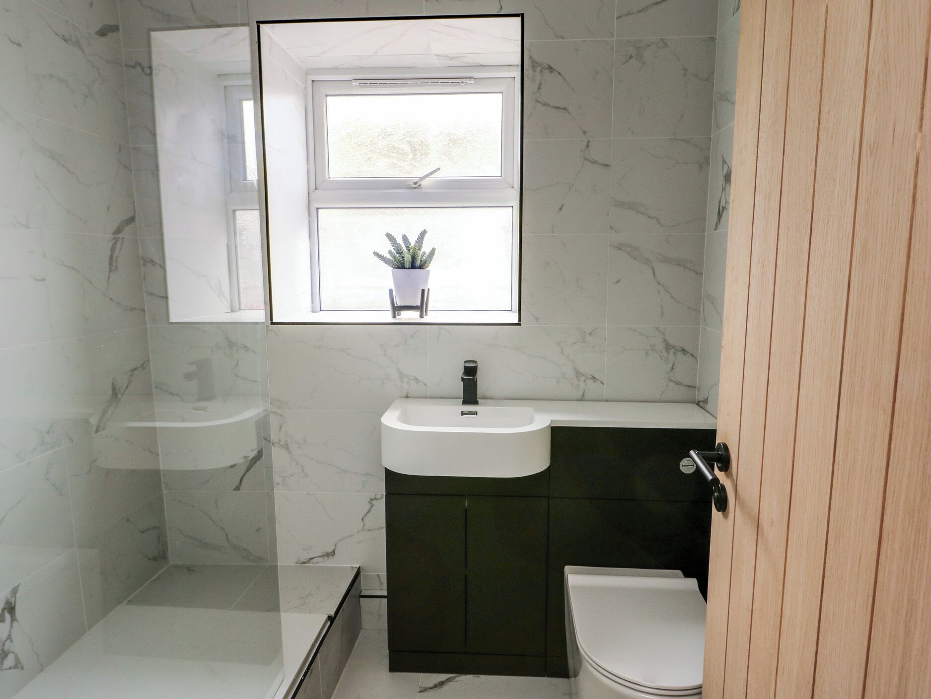 A bathroom with a white sink, dark cabinet, and a window with a potted plant.