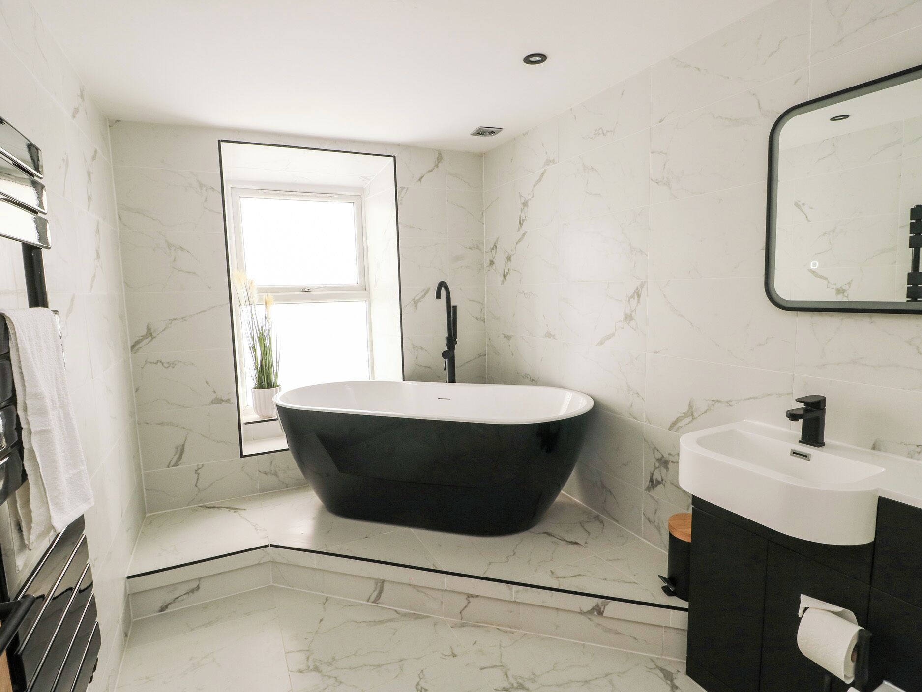 Un baño moderno con una bañera independiente, un lavabo y un espejo grande.