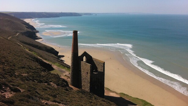 A coastal landscape with a beach, a cliff, and a historical stone structure. - Skylarks! (St. Agnes)