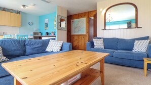 A living room with a wooden coffee table, two blue sofas, a kitchen area with wooden cabinets, and a map on the wall. - Skylarks! (St. Agnes)