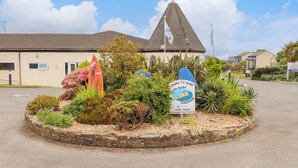 A coastal building with a pointed roof, surrounded by a landscaped garden with various plants and a surfboard sign. - Skylarks! (St. Agnes)