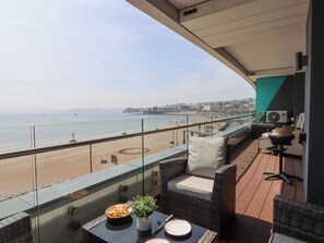 A balcony with a view of the beach, wicker furniture, a table with plates and a bowl of food, and an air conditioning unit.