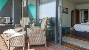 Una habitación moderna con balcón, muebles de mimbre, una cama y un ventanal grande.
