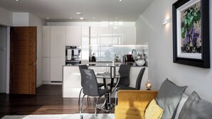 Una cocina moderna con armarios blancos, un comedor con mesa de vidrio y un sofá amarillo.