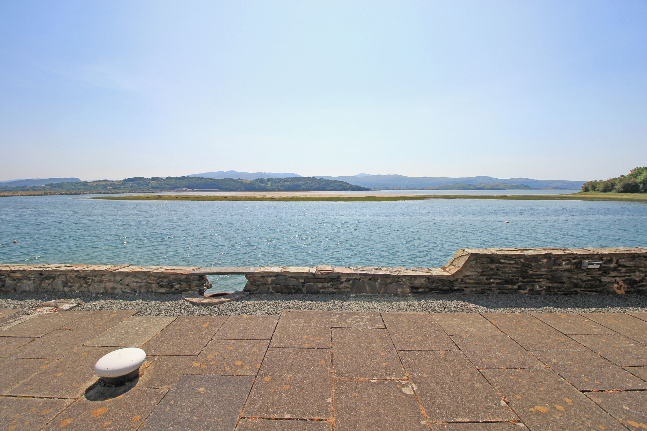 Eine Uferpromenade aus Stein mit Blick auf einen stillen See und entfernte Berge.
