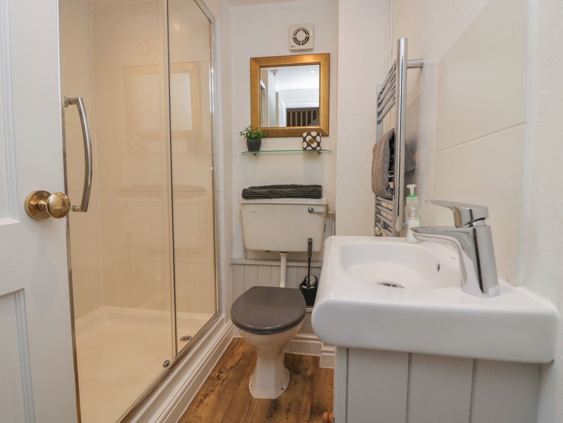 Een moderne badkamer met een douchecabine van glas, een toilet, een wastafel met zeepdispenser en een spiegel boven de wastafel.