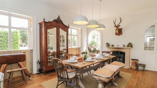 Ein Esszimmer mit Holztisch, gedeckt für vier Personen, umgeben von Stühlen, einem Kamin und einem Hirschkopf an der Wand.