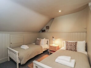 A bedroom with two single beds, a nightstand with a lamp, and a small shelf with a picture. - Cotswold House (Moreton-in-Marsh)