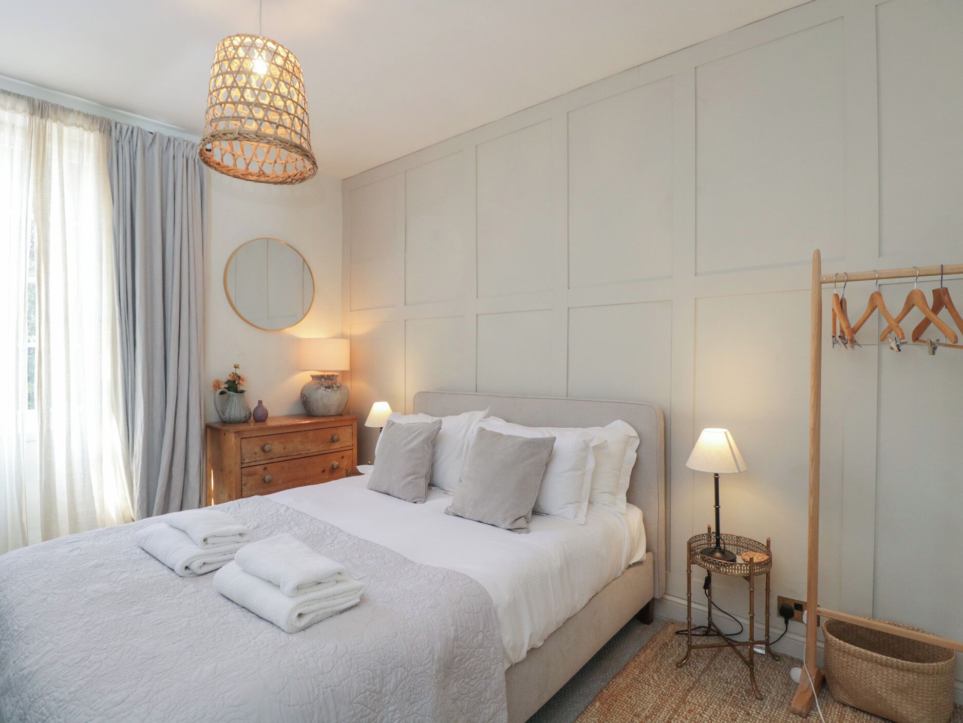 Un dormitorio ordenado con cama, lámparas de noche, una lámpara colgante, un espejo y un aparador de madera.