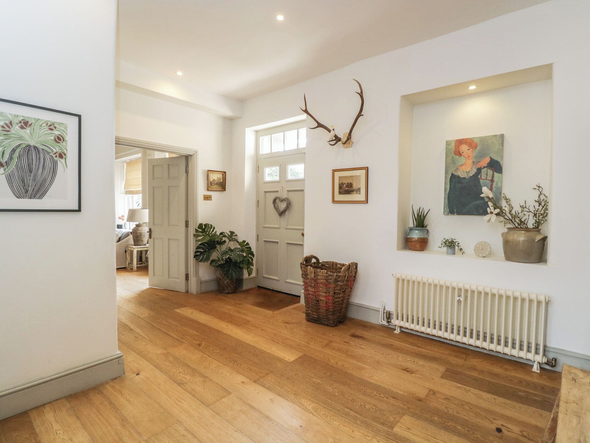 A hallway with wooden flooring, a white door, a wall-mounted antler decoration, and a framed painting.