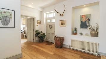 A hallway with wooden flooring, a white door, a wall-mounted antler decoration, and a framed painting.