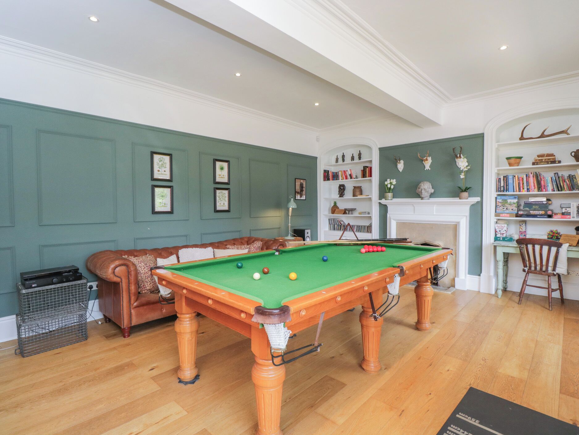 Una sala de billar con mesa de pool, sofá de cuero, chimenea y estanterías.