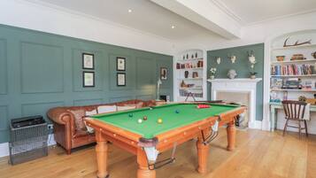 Una sala de billar con mesa de pool, sofá de cuero, chimenea y estanterías.