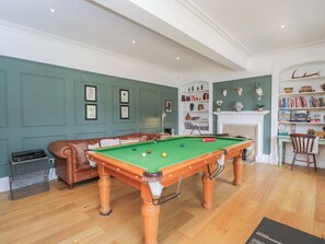 Una sala de billar con mesa de pool, sofá de cuero, chimenea y estanterías.