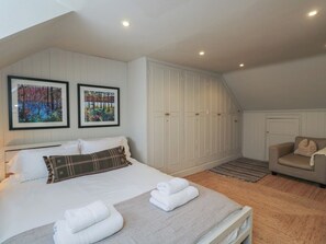 A bedroom with a bed, two framed pictures, a wardrobe, a sofa, and a carpeted floor.