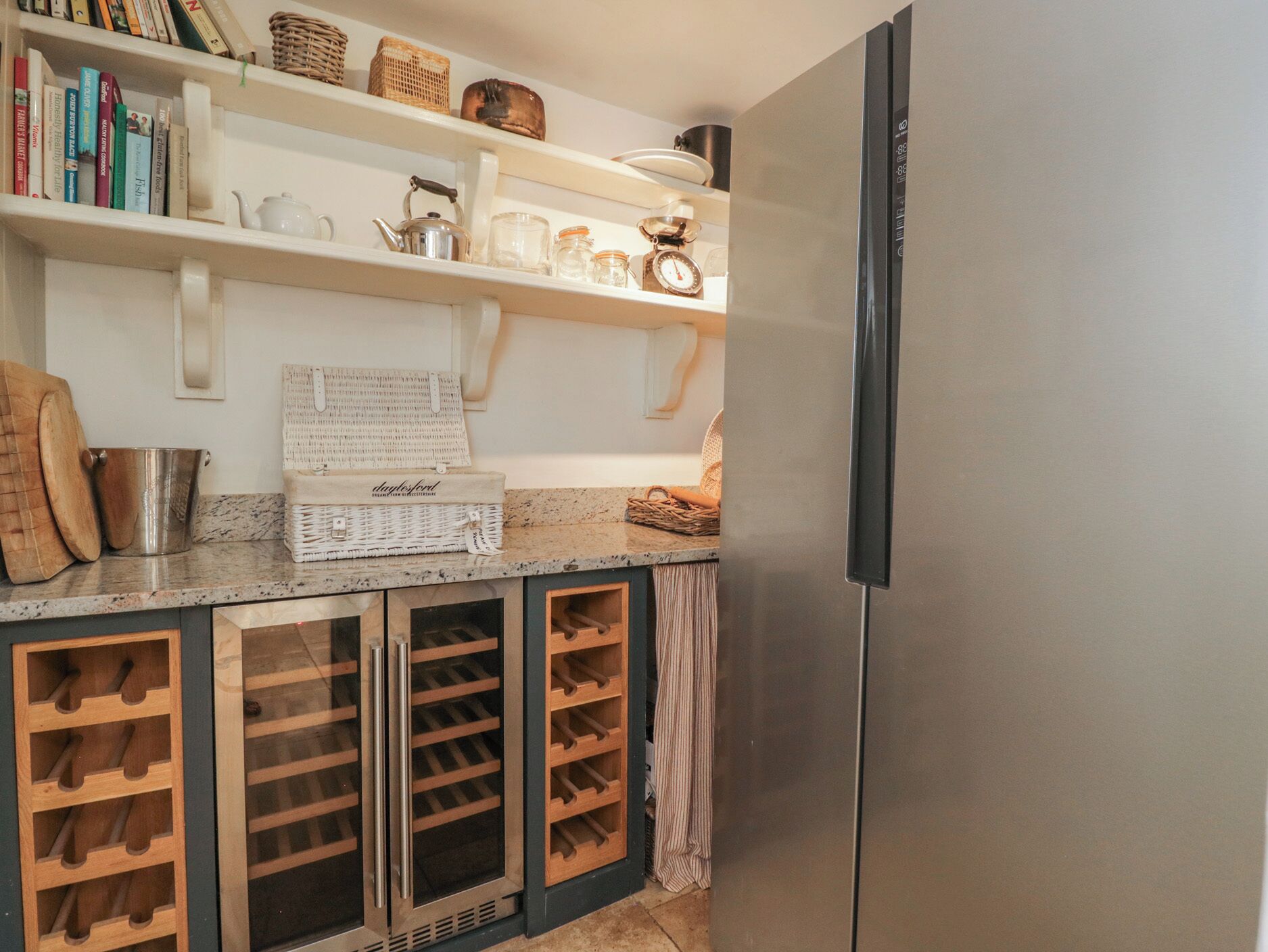 Una cocina con refrigerador de acero inoxidable, almacenamiento para vinos, una cafetera y una repisa con libros y utensilios de cocina.
