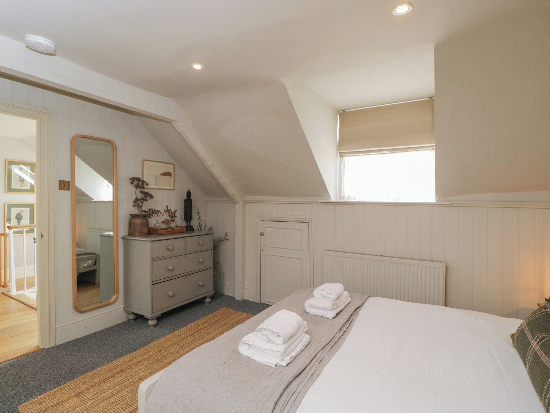 A bedroom with a bed, a dresser, a mirror, and a window.