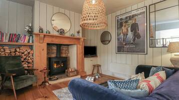 Uma sala de estar acolhedora com lareira, um sofá confortável, uma estante de livros e um cartaz de filme na parede.