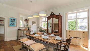 Uma sala de jantar com mesa de madeira posta para quatro pessoas, um espelho grande e luminárias pendentes.