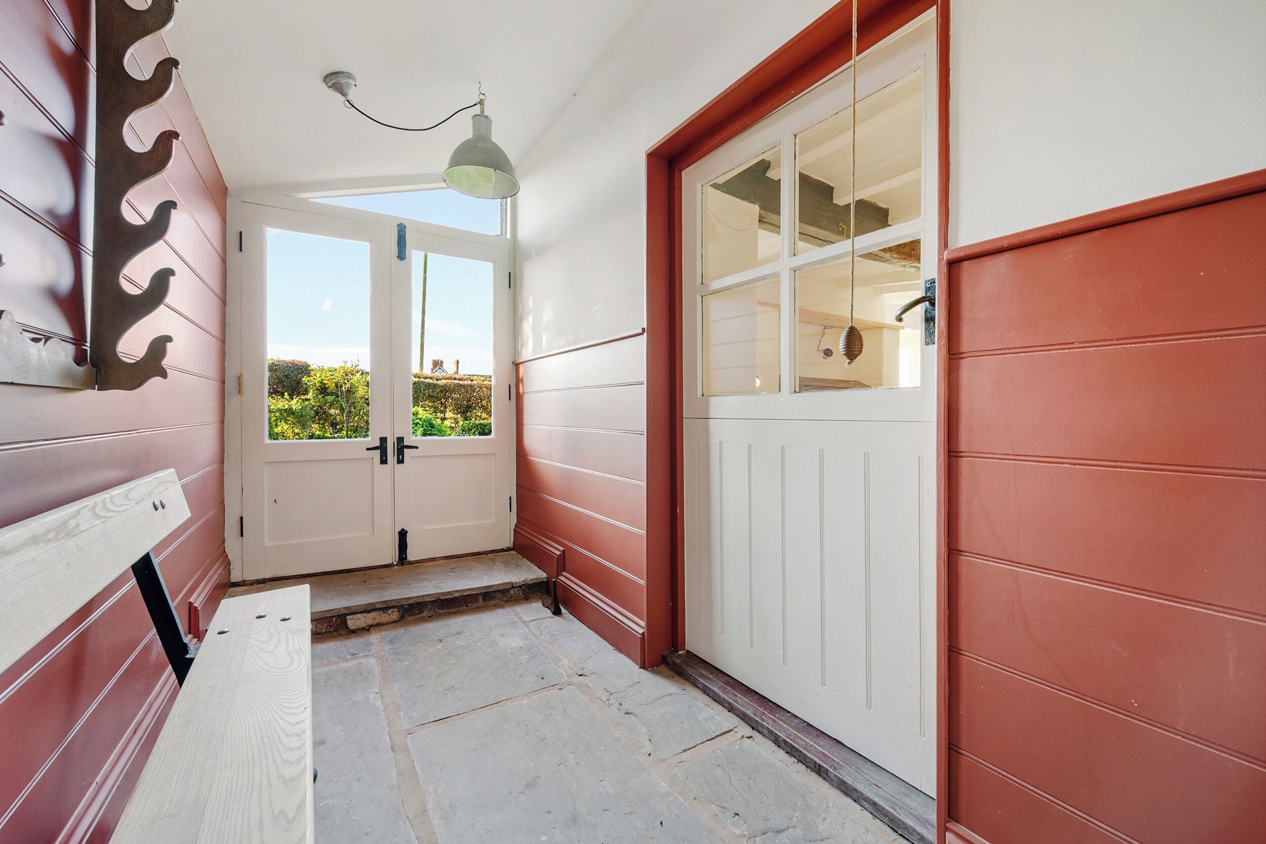 A hallway with a bench, a door, and a window with a view of greenery.