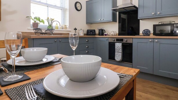 A modern kitchen with grey cabinets, a black stove, and a microwave on the countertop. - Elm Tree Cottage (Thirsk)