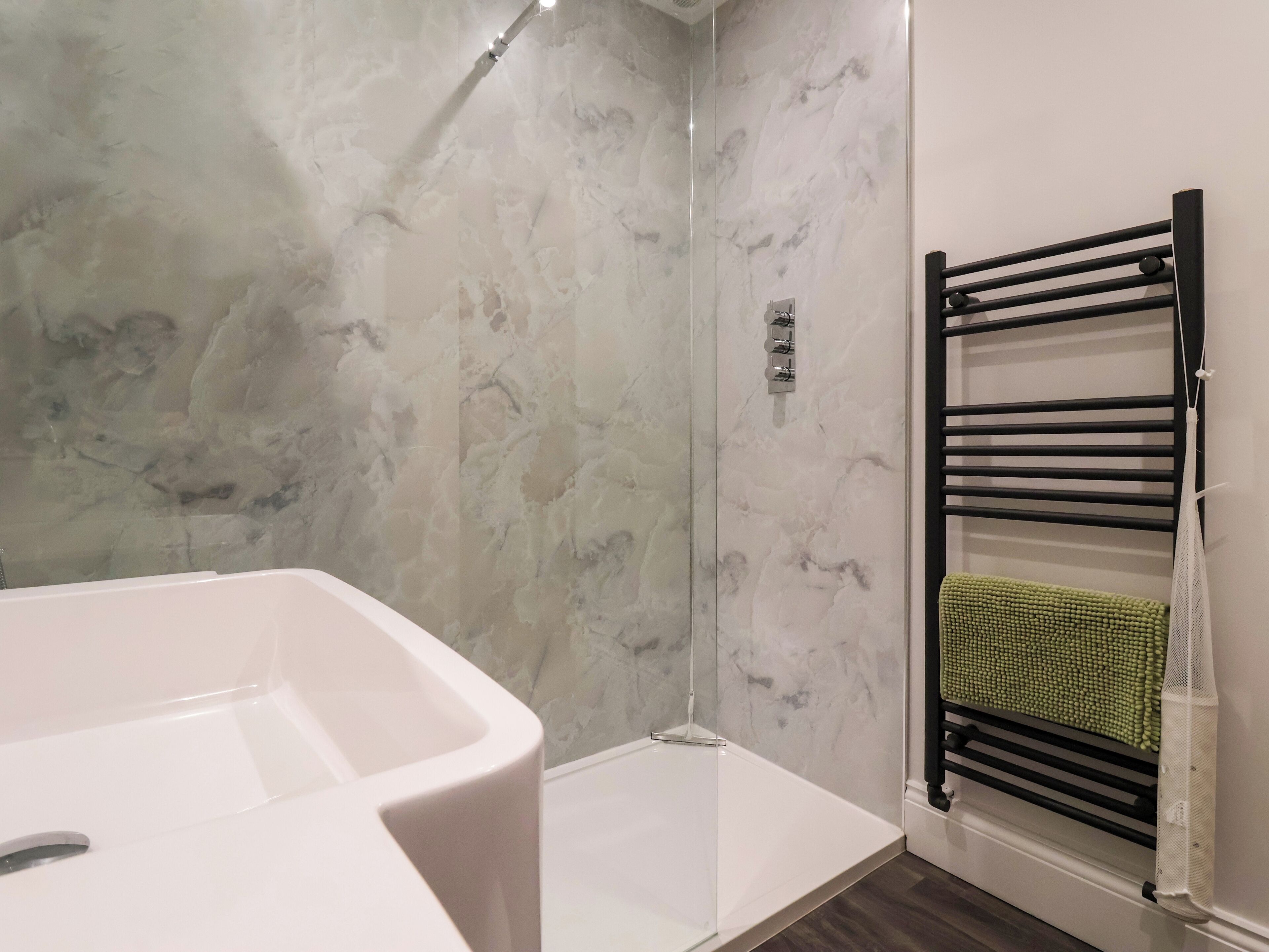 A bathroom with a white bathtub, a glass-enclosed shower, and a black towel rack with a green towel.