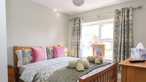 A neatly made bed with floral bedding, a wooden headboard, and a bedside table with a lamp. - Elm Tree Cottage (Thirsk)