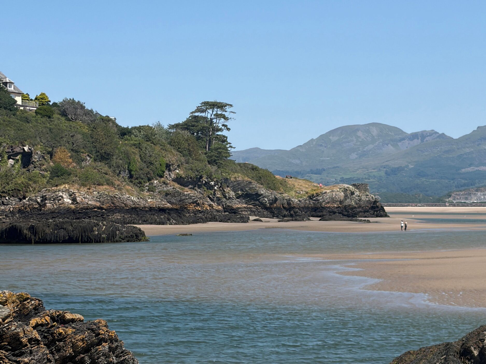 Eine Küstenlandschaft mit felsigen Ufern, einem Sandstrand und einem Berg im Hintergrund.
