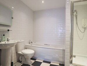 A bathroom with white tiled walls, a sink, a toilet, and a bathtub. - The Quarterdeck (Porthmadog)