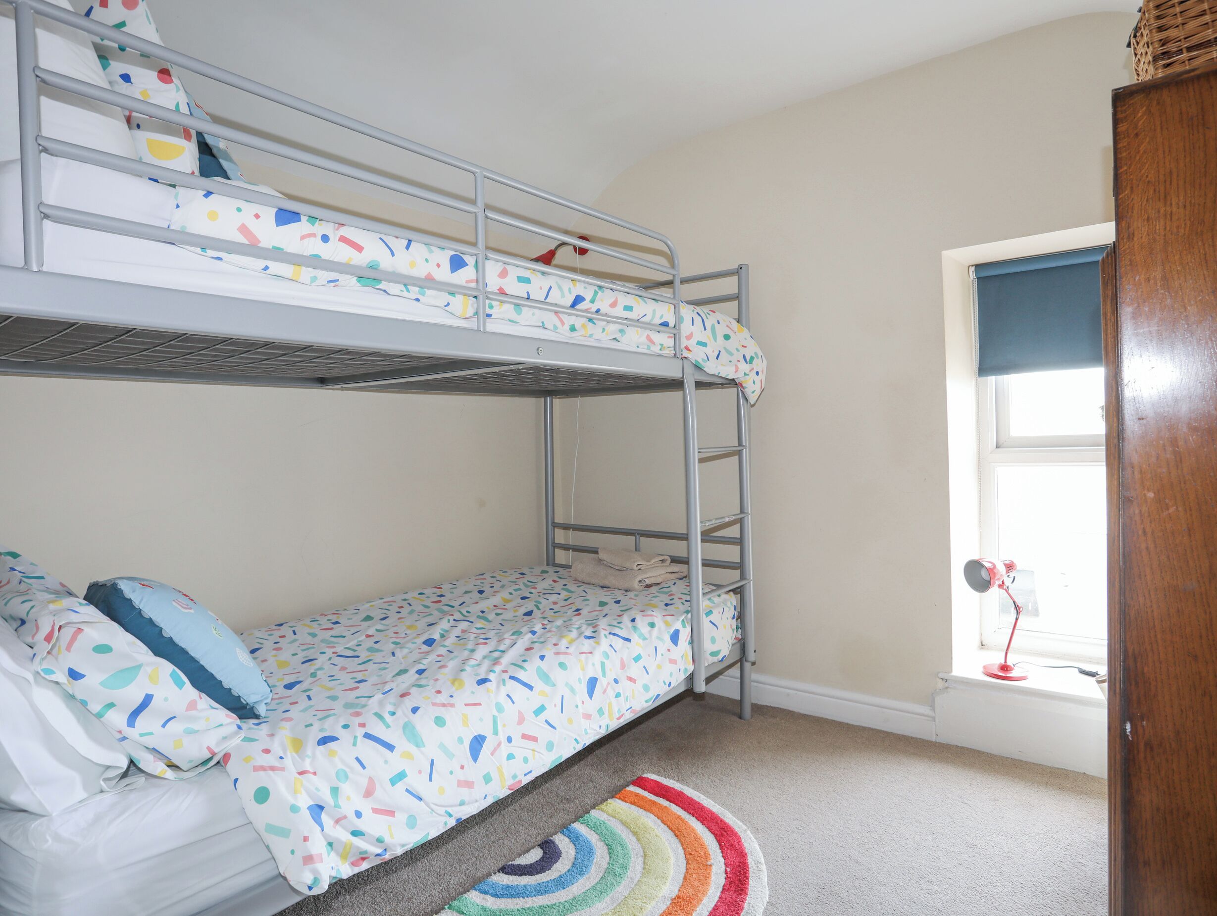 A bunk bed room with a window, a radiator, and a colorful rug.