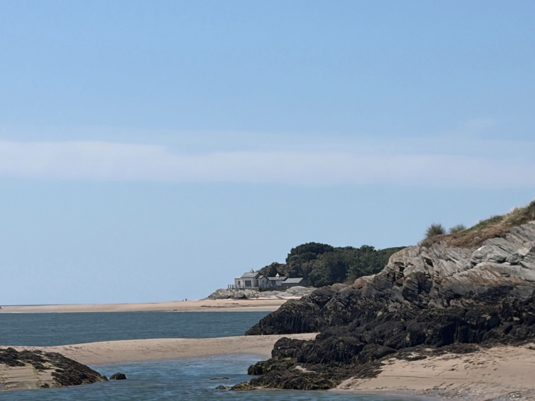 A coastal property with a beach, rocky cliffs, and a clear sky.