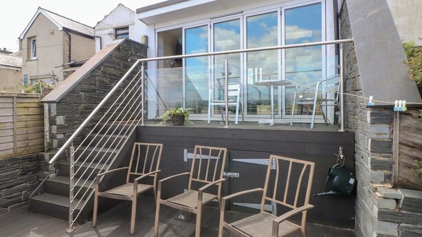 Une maison moderne avec une façade en pierre, une porte en verre et un petit espace extérieur aménagé avec deux chaises.