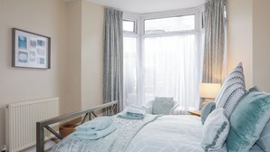 Une chambre à coucher avec un lit, une chaise, un radiateur et une fenêtre avec des rideaux.