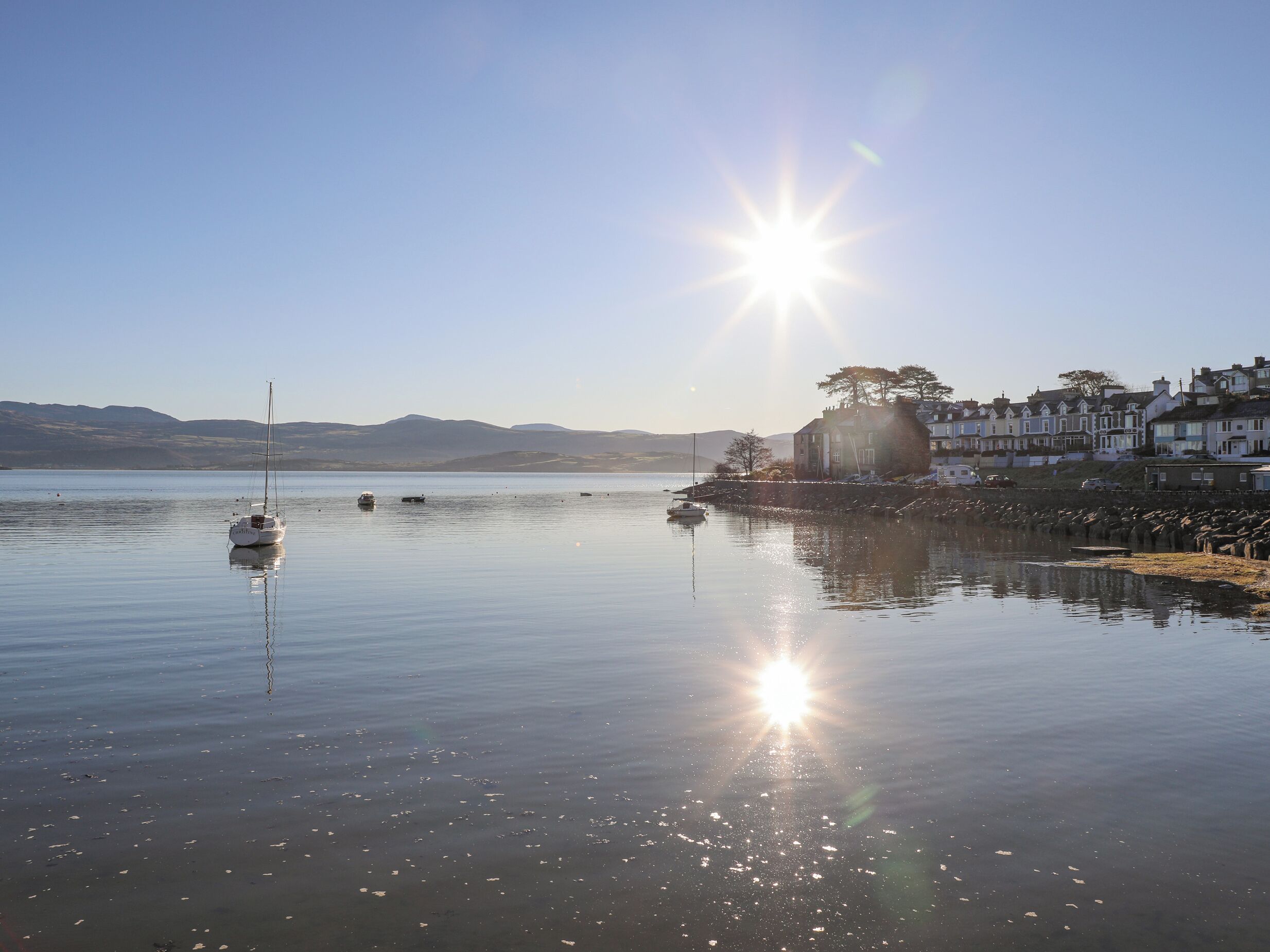 Un port tranquil amb vaixells, un cel serè i una filera de cases al costat de la riba.